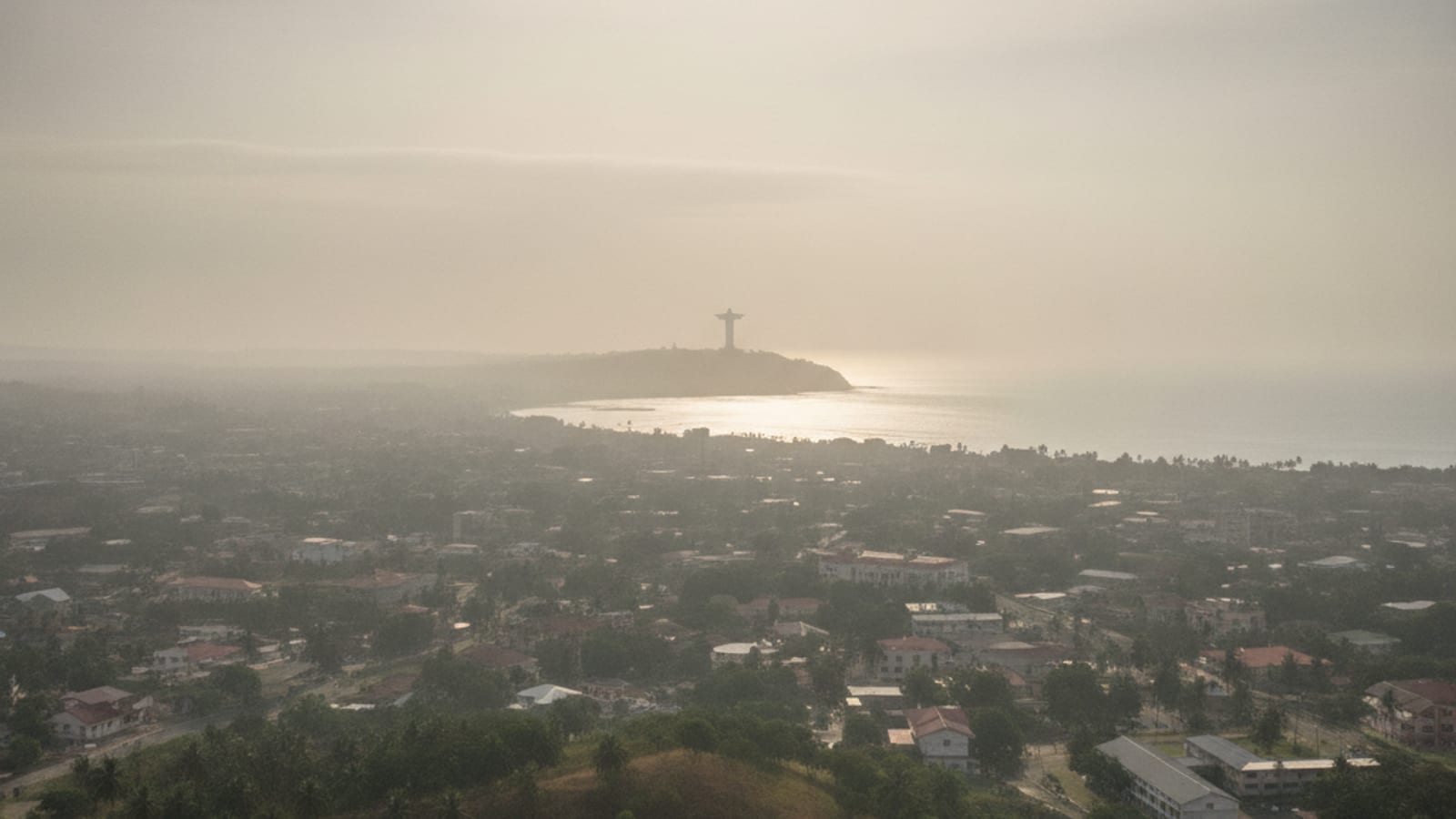 Dili city skyline with a faint haze, showing the Cristo Rei statue on the horizon.