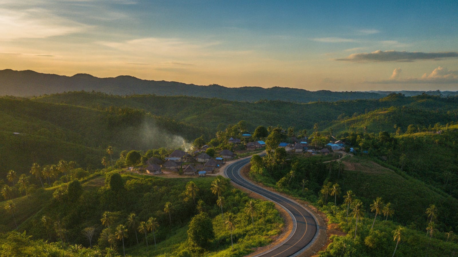 A smooth, newly constructed road winding through the lush, green landscape of rural Timor-Leste, with a village in the background.