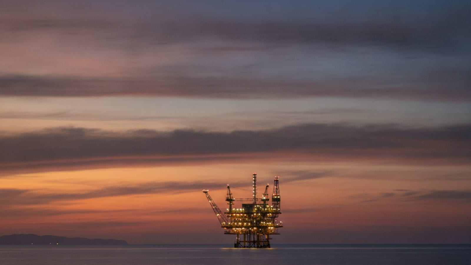 A distant offshore oil and gas platform on a calm sea at dusk