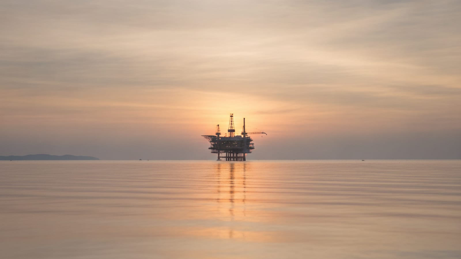 A distant offshore oil and gas platform on a calm sea at dawn