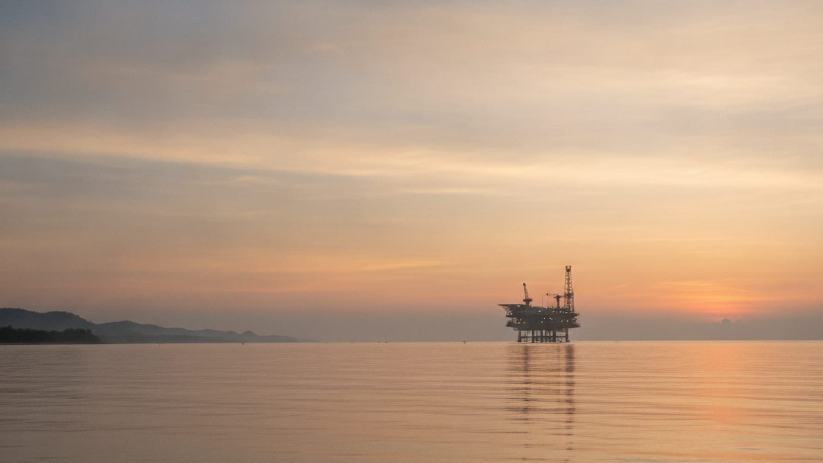 A calm sea with a distant offshore platform at sunrise